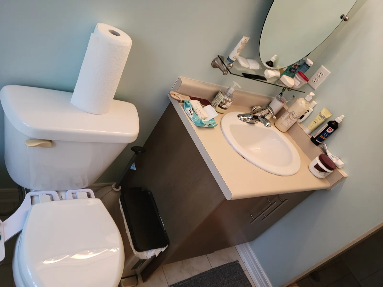 Old oval-sink vanity and builder mirror in the Aurora bathroom before renovation