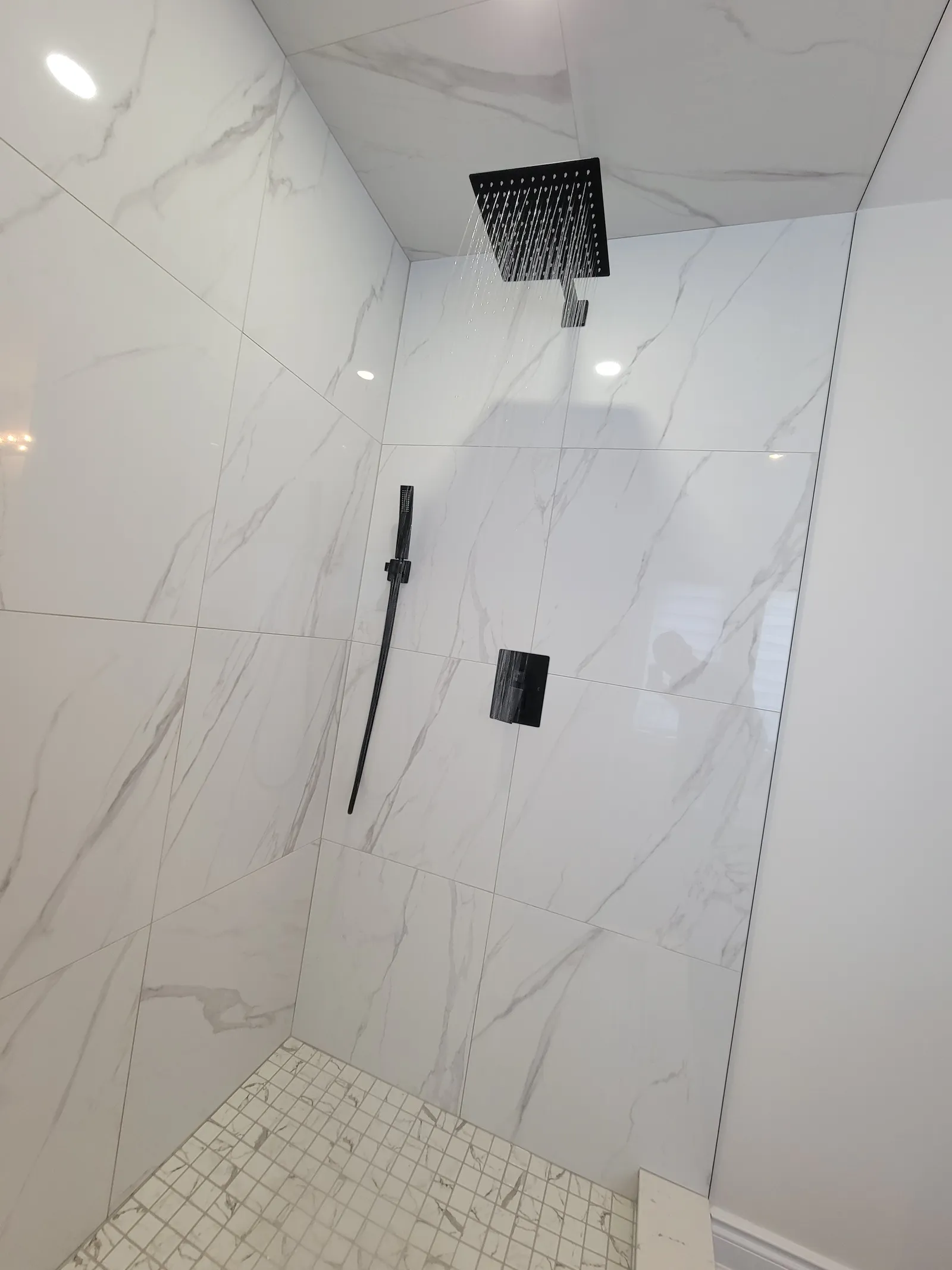 Wide view of the finished Vaughan walk-in shower showing the black hand shower, slide bar and white mosaic accent column