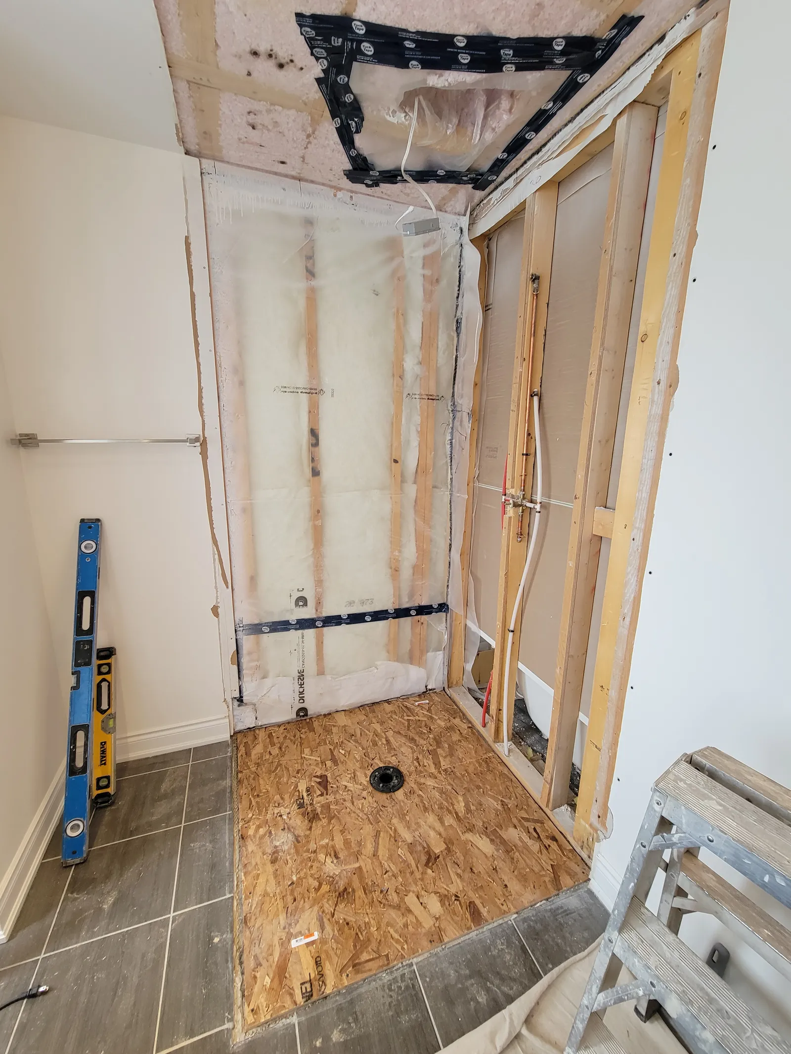 Vaughan shower stripped to the wood studs during rough-in, with copper and PEX supply lines and a drain flange in the subfloor